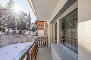 A balcony with a wooden railing, a view of snow-covered ground, and a building with a large window. - Breathtaking Luxury Stay, Wallis 1079 (Wallis)