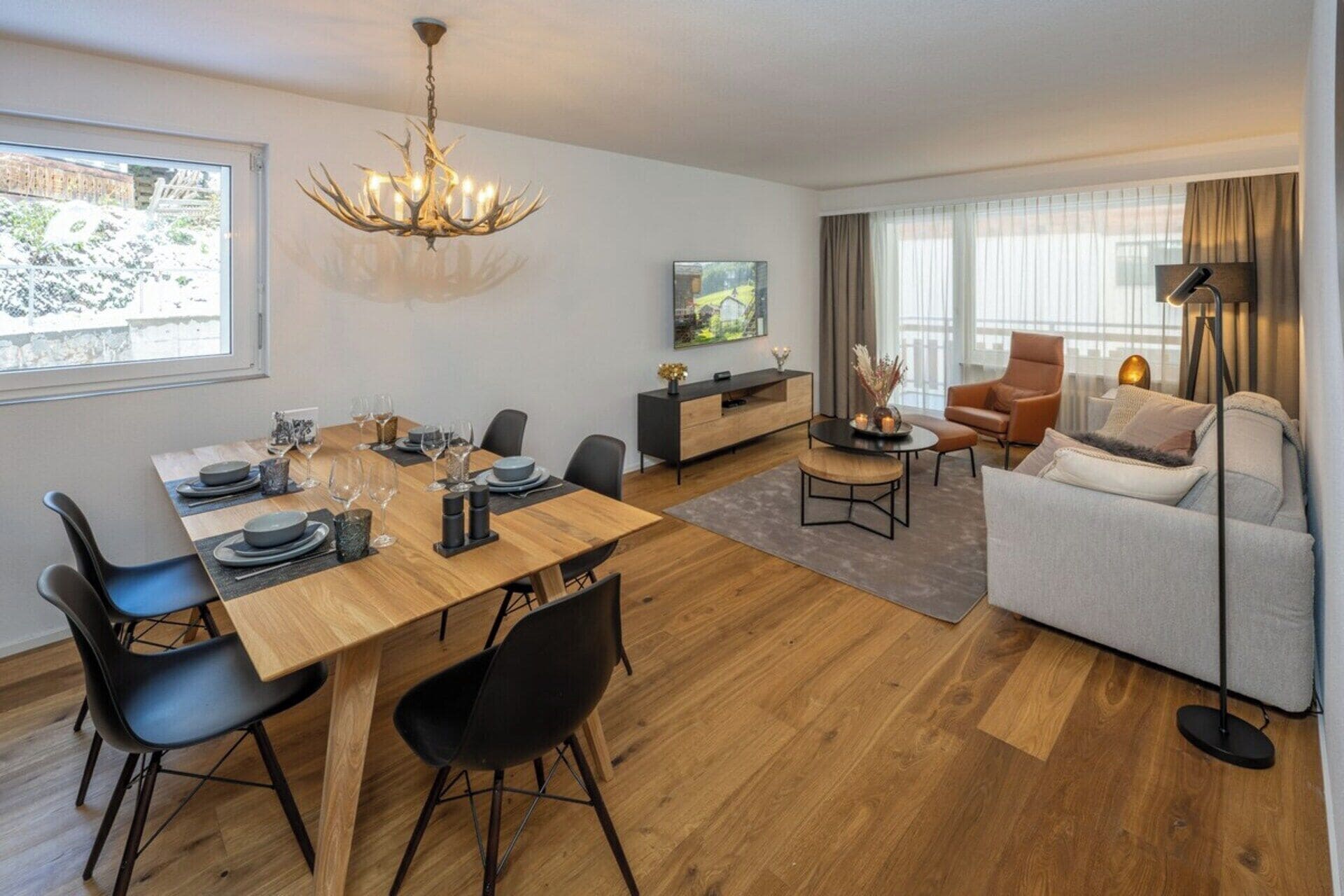 A modern living room with a dining area, a sofa set, a television, and a chandelier.