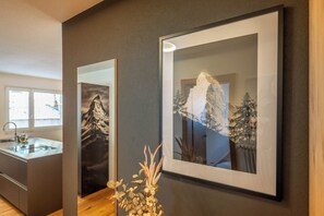 A modern interior with a framed artwork of a mountain and trees, a wooden cabinet, and a vase with dried plants. - Breathtaking Luxury Stay, Wallis 1079 (Wallis)