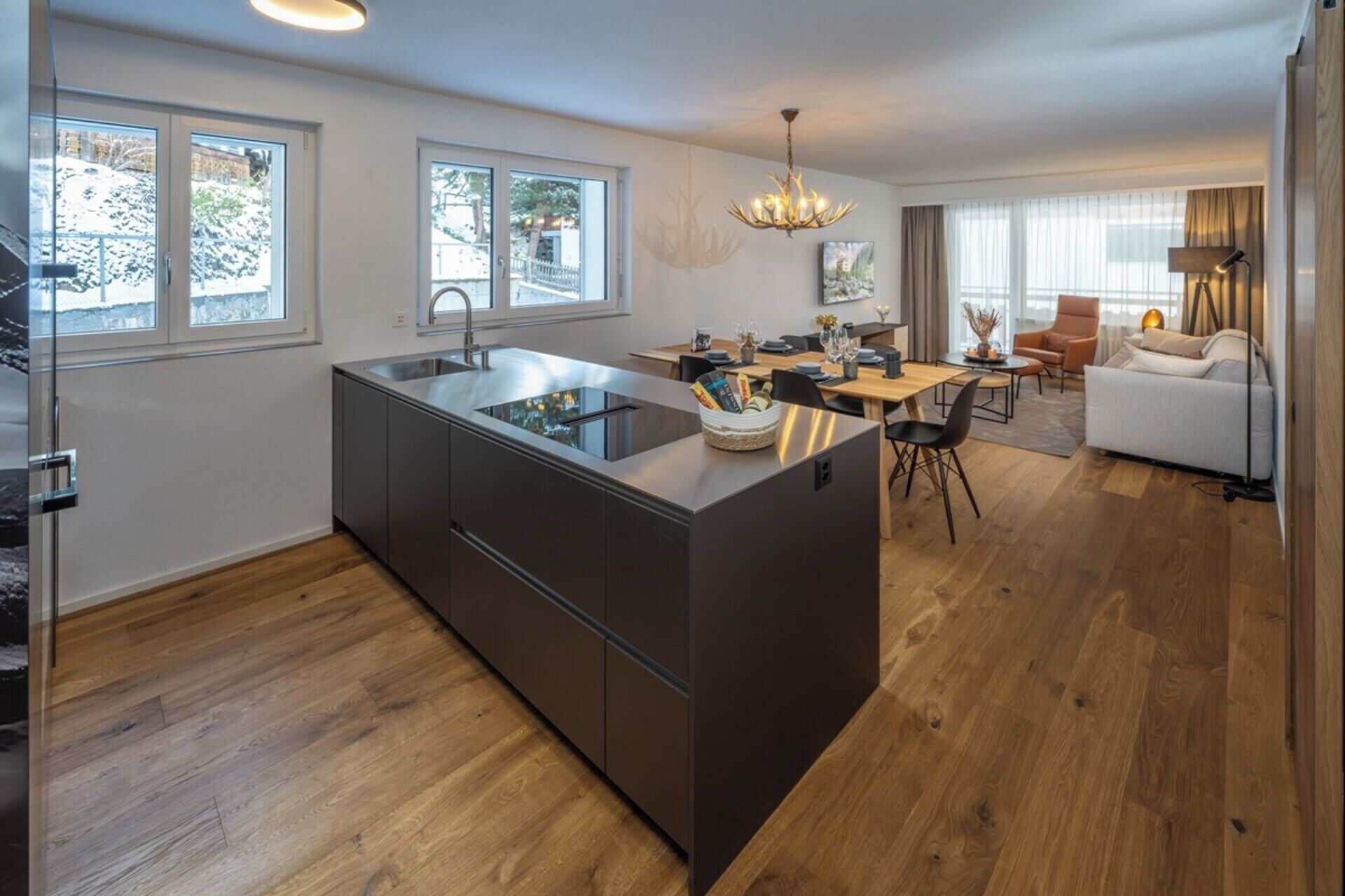 A modern kitchen with a central island, a dining area with a table and chairs, and a living room with a sofa and a lamp.