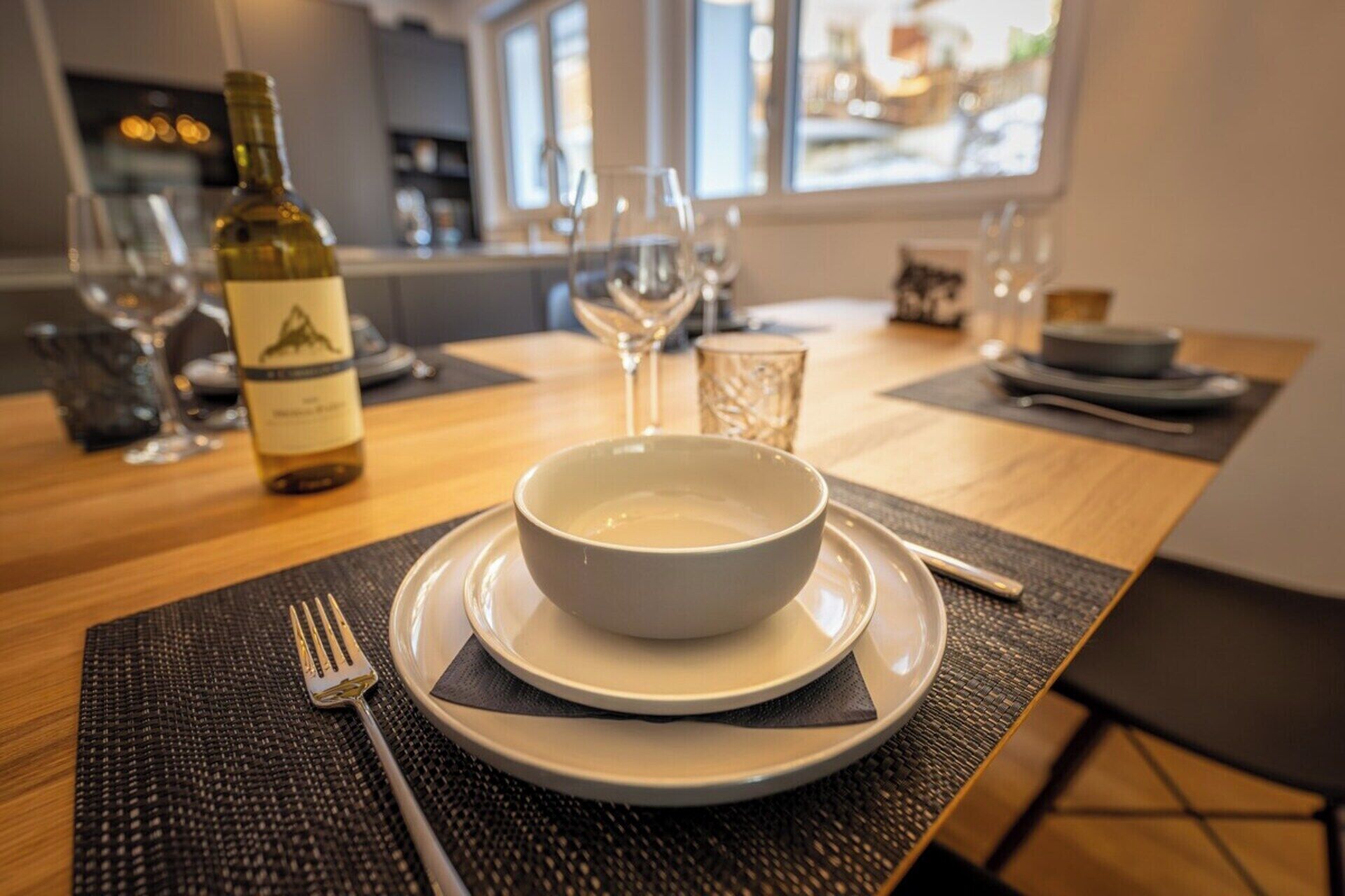 A dining table with a bowl of soup, a wine bottle, and glasses.