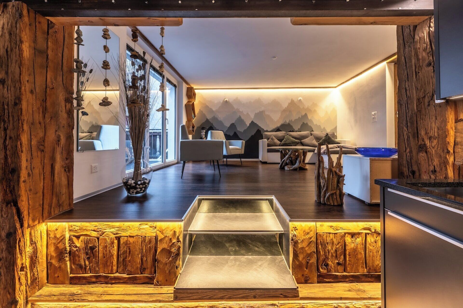Un intérieur moderne avec un mur d’accent en bois, un coin salon avec un canapé et des fauteuils, et une table à manger agrémentée d’un saladier bleu.