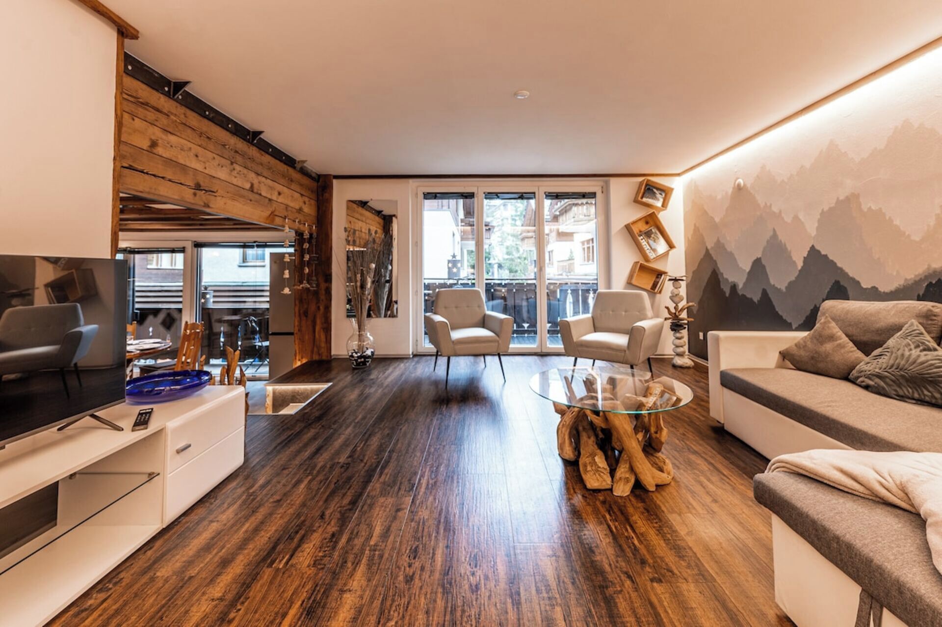 Un salon moderne avec un plancher en bois, une table basse en verre, un canapé et un téléviseur posé sur un meuble.