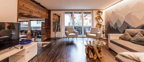 A modern living room with a wooden floor, a glass coffee table, a sofa, and a TV on a stand.