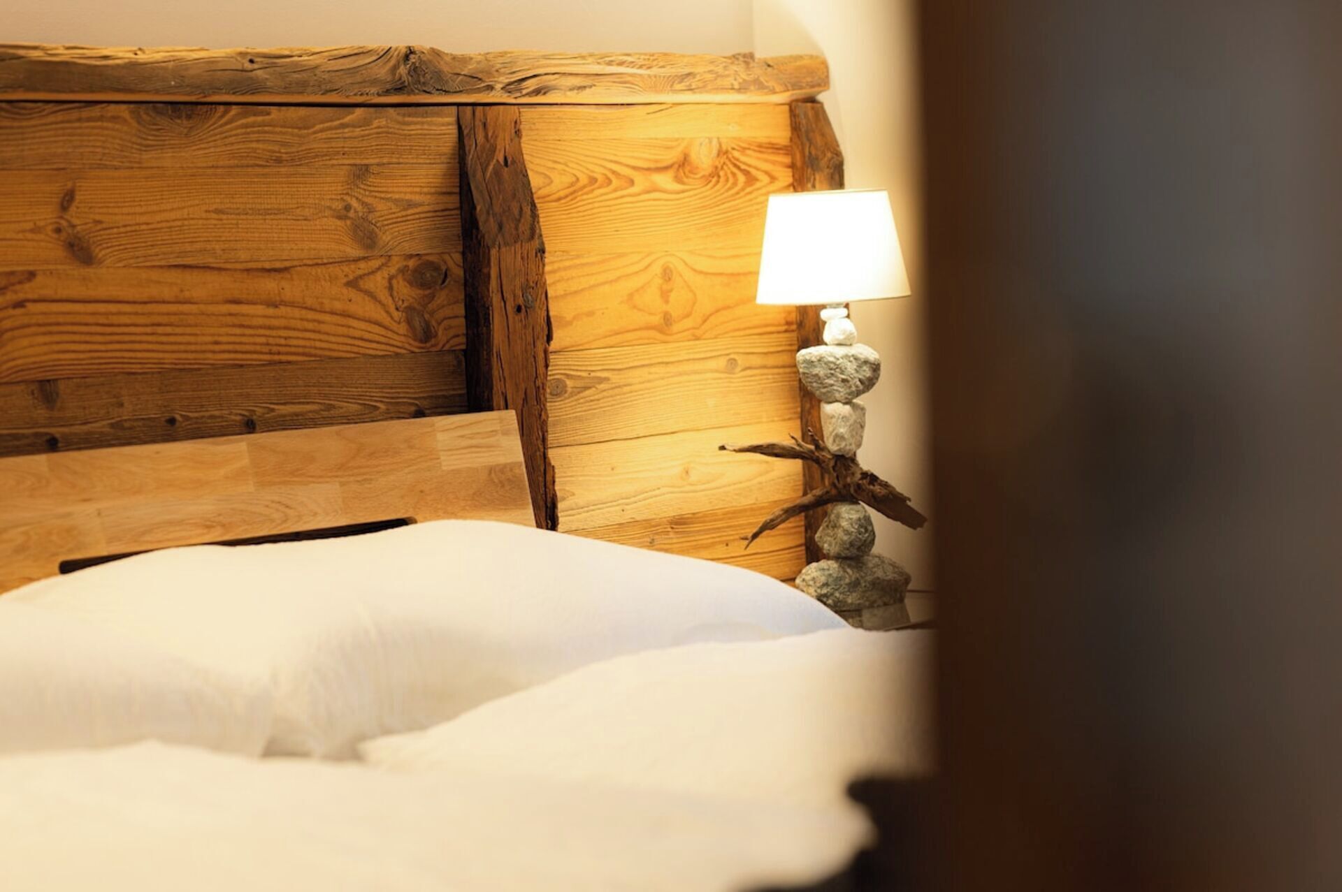 A wooden headboard, a white pillow, and a lamp with a rock decoration.