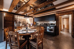 Ein Essbereich mit einem runden Tisch, gedeckt für vier Personen, Holzstühle und eine Küche mit modernen Geräten.