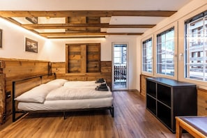 Ein Zimmer mit Holzboden, einem Bett mit weißer Bettwäsche, einem Holz-Kopfteil, einer Schiebeglastür und einem großen Fenster.