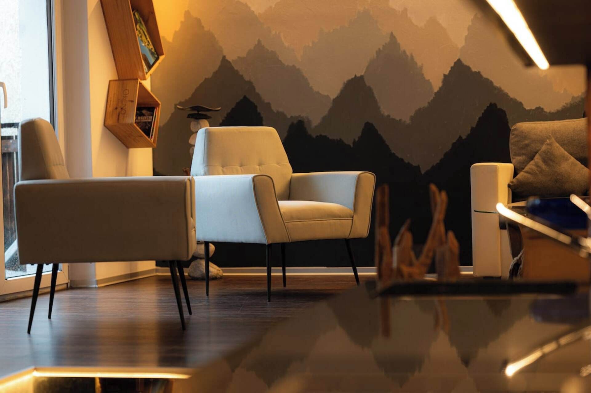 Ein modernes Wohnzimmer mit einer Couch, einem Sessel und einer Wand mit Bergmotiv.
