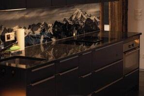 Eine moderne Küche mit einer Granit-Arbeitsplatte, Edelstahlgeräten und einer Rückwand mit einer Berglandschaft.
