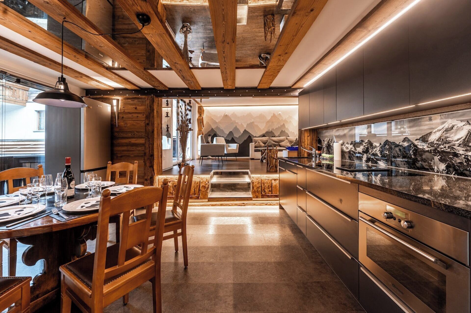 Une cuisine moderne avec des poutres en bois, des appareils électroménagers en acier inoxydable et un mur décoré sur le thème de la montagne.