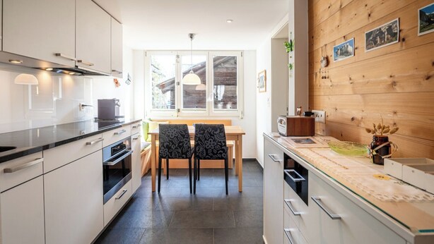 A modern kitchen with white cabinetry, a wooden wall with framed pictures, and a dining area with a bench and chairs. - Where Comfort Meets Luxury, Wallis 1081 (Wallis)