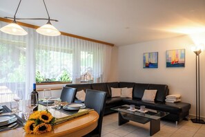 Un salon moderne avec un canapé en cuir noir, une table basse en verre et un coin repas avec une table en bois mise pour deux personnes.