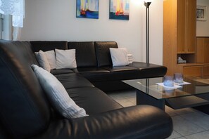 Un salon moderne avec un canapé en cuir noir, une table basse en verre et des œuvres d’art accrochées au mur.