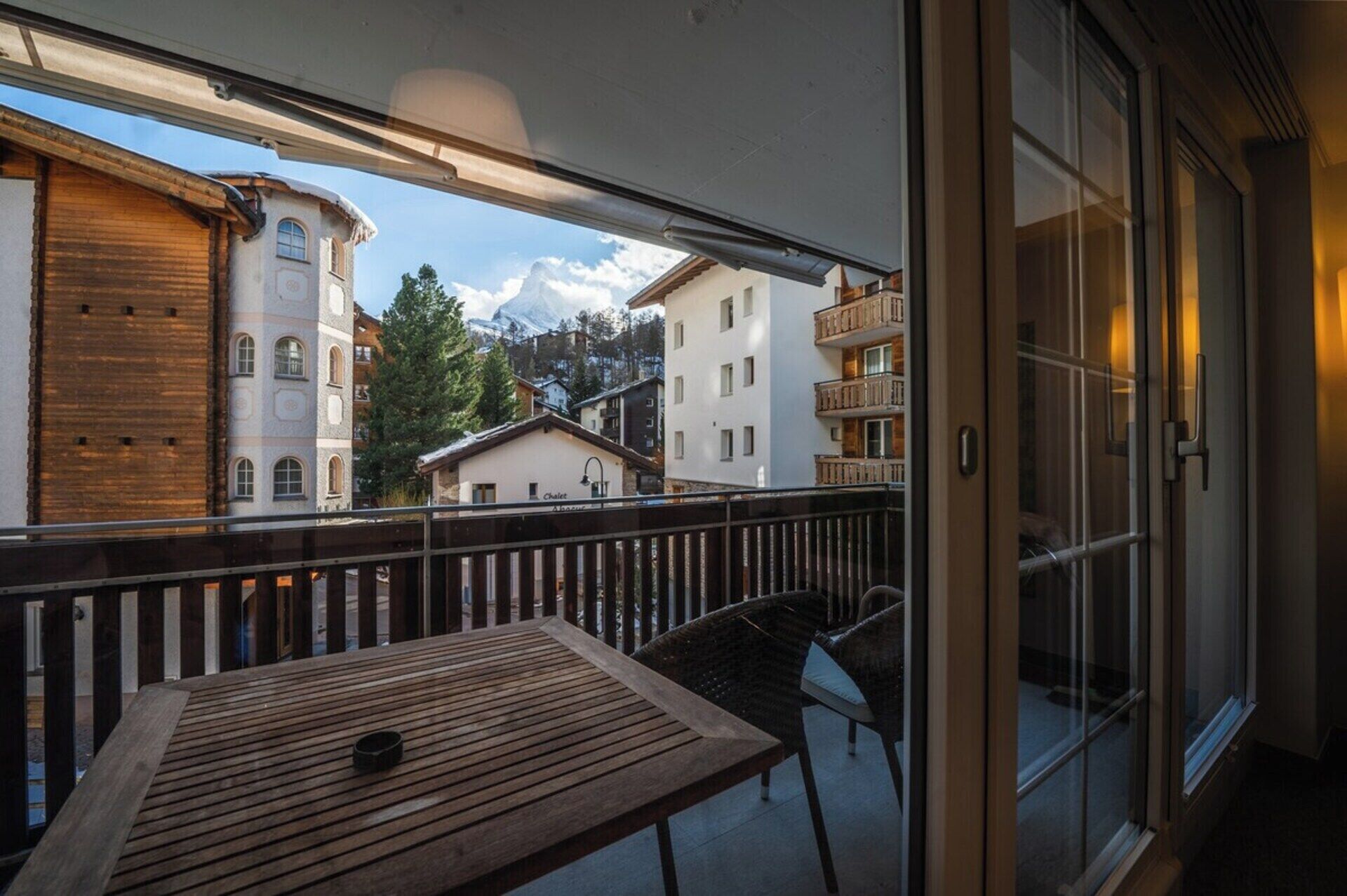 A balcony with a wooden table and chairs, overlooking a mountain and buildings.