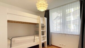 Ein Schlafraum mit Etagenbetten, einer Leiter, einem Fenster mit Vorhängen und einer Lampe.