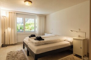 A bedroom with two beds, a bedside table, a lamp, and a window with curtains. - Mountain Bliss Awaits, Wallis 1075 (Wallis)