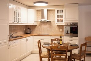 Una cocina con armarios blancos, horno empotrado y una mesa de comedor con sillas.