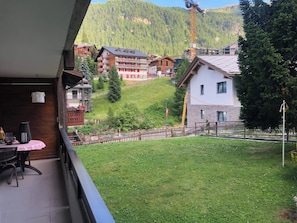 Un balcón con una mesa y sillas, con vista a un césped verde y una colina con edificios.
