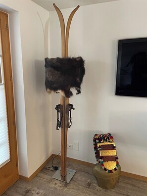 Ein Zimmer mit einem Holz-Kleiderständer, einem an der Wand montierten Fernseher und einem dekorativen Sessel mit farbigem Kissen.