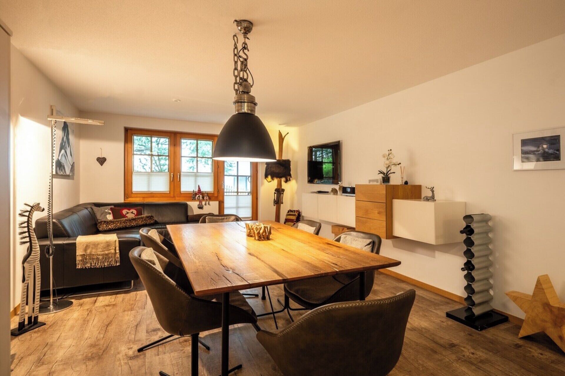 Ein Essbereich mit Holztisch und -stühlen, einer Couch und einem Fernseher an der Wand.