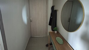 Ein schmaler Flur mit einer hölzernen Bank, einem runden Spiegel und einer Tür am Ende.