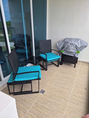 Ein Balkon mit zwei Stühlen, einem Tisch, einem überdachten Grill und einer Glasdoor, die nach draußen führt.