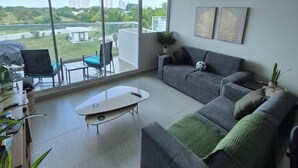 Ein modernes Wohnzimmer mit grauem Sofa, einem Couchtisch und einem großen Fenster mit Blick auf Grünflächen und Gebäude.