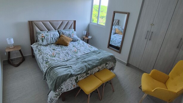 Ein Schlafzimmer mit einem Bett, Nachttischen, einem Spiegel, einem Kleiderschrank und einem Fenster.