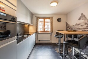 Eine kompakte Küche mit Fenster, ein Essbereich mit Barhocker und einer an der Wand befestigten Uhr.