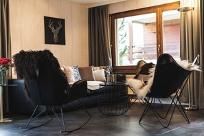 Ein modernes Wohnzimmer mit einer Couch, zwei schwarzen Sesseln, einem runden Couchtisch und einem dekorativen Wandbild.