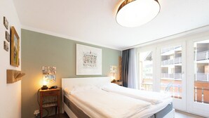 Ein Doppelbett mit grauem Lattenrost, ein Nachttisch mit Lampe und eine Wand mit gerahmten Bildern.