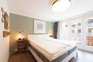 Ein Doppelbett mit grauem Lattenrost, ein Nachttisch mit Lampe und eine Wand mit gerahmten Bildern.
