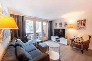 Ein modernes Wohnzimmer mit einer Couch, einem Couchtisch, einem Fernseher und einem Sessel.