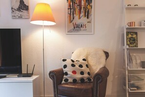 A living room with a brown leather armchair, a polka dot pillow, a standing floor lamp, a flat-screen TV, and a bookshelf with various items. - LuxuryYour Luxury Alpine Escape, Wallis 1070 (Wallis)