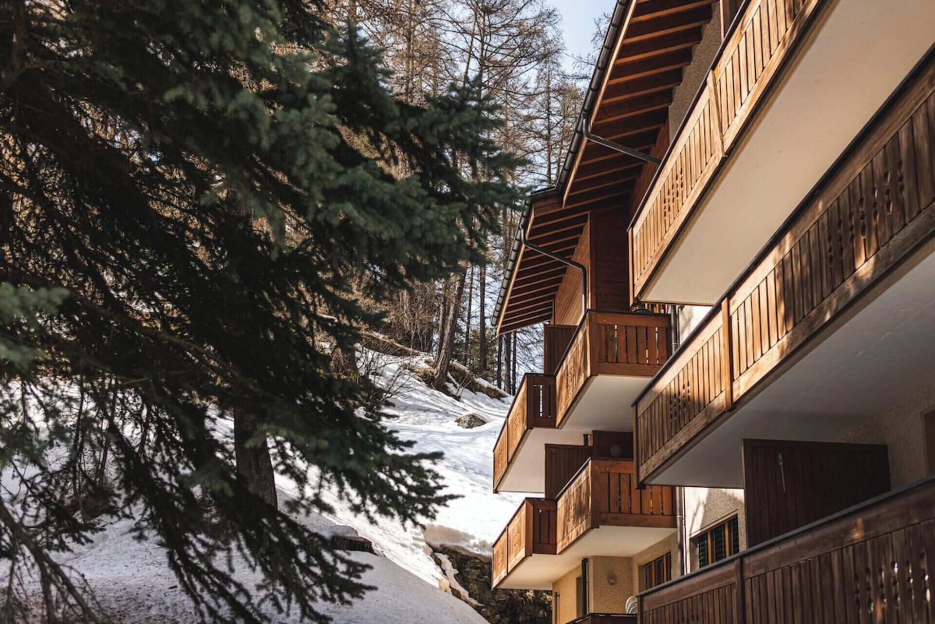 A multi-story building with wooden balconies, surrounded by trees and snow.