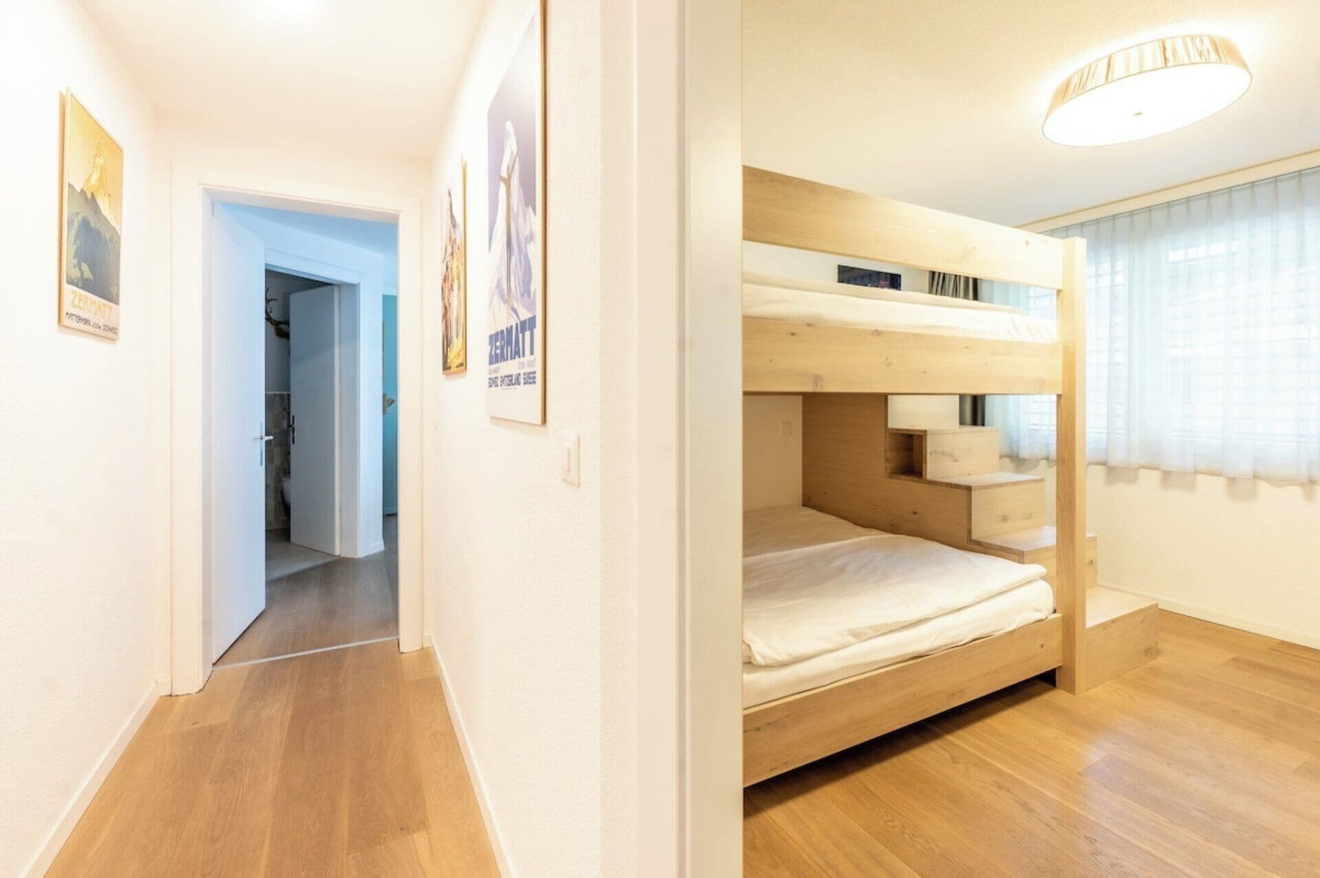 Een kamer met een stapelbed, houten vloer, een deur naar een andere kamer en een poster aan de muur.