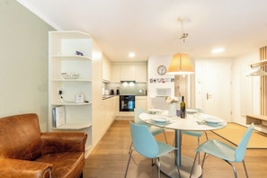 A modern kitchen with white cabinets, a dining area with a round table and blue chairs, and a brown leather sofa. - LuxuryYour Luxury Alpine Escape, Wallis 1070 (Wallis)