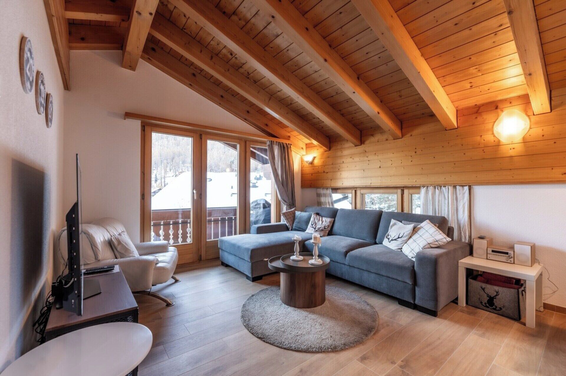 Ein gemütliches Wohnzimmer mit Holzbalkendecke, einer Couch, einem Couchtisch und einem Fernseher.