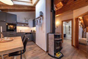 A modern kitchen with a built-in oven, a dining area with a wooden table and chairs, and a wood-burning stove. - Luxury Alpine Retreat, Wallis 1071 (Wallis)