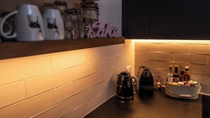 Ett kök med en hylla där det står muggar och burkar, en kaffebryggare och ett kryddställ.