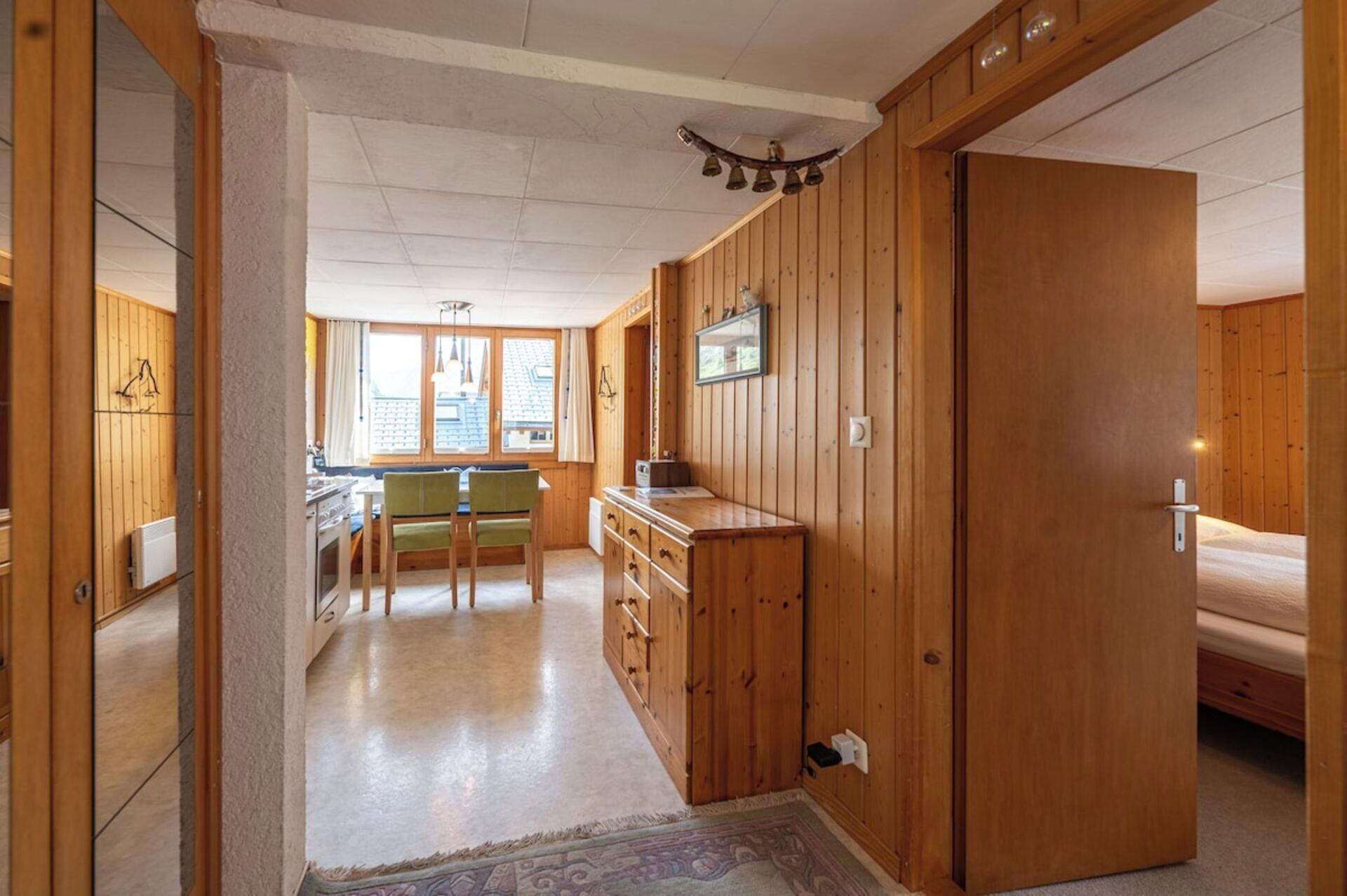 A wooden-paneled room with a kitchenette, a dining area, and a bed.