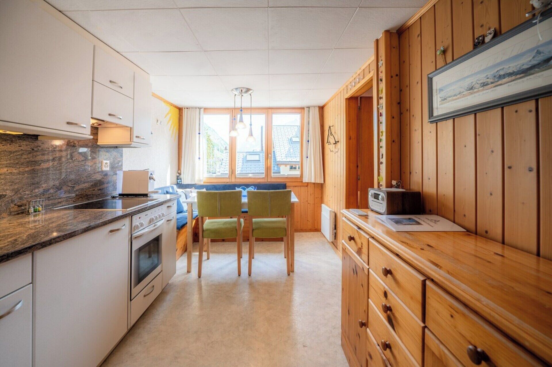 Une cuisine compacte comprenant un coin repas, des meubles en bois, un four à micro-ondes et une fenêtre laissant entrer la lumière naturelle.
