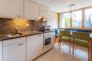 Eine moderne Küche mit Granit Arbeitsplatte, Edelstahlspüle und weißen Schränken. Ein eingebauter Backofen und ein Essbereich mit blauem Sofa und grünen Stühlen sind vorhanden.