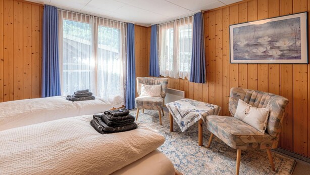 Una habitación de hotel con una cama grande, dos sillones, un cuadro en la pared y una ventana con cortinas.