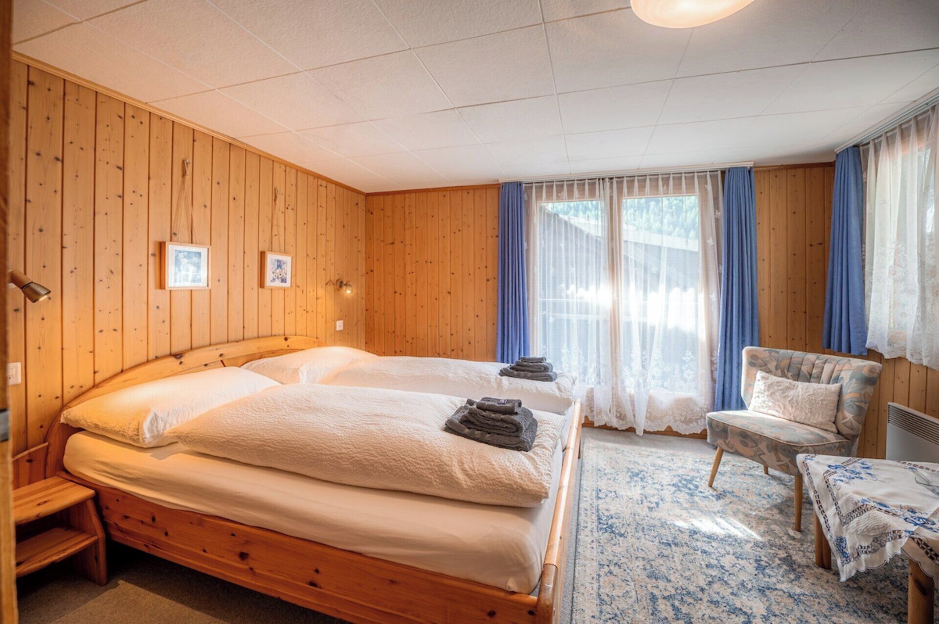 A room with two beds, a chair, a table, and a window with curtains.