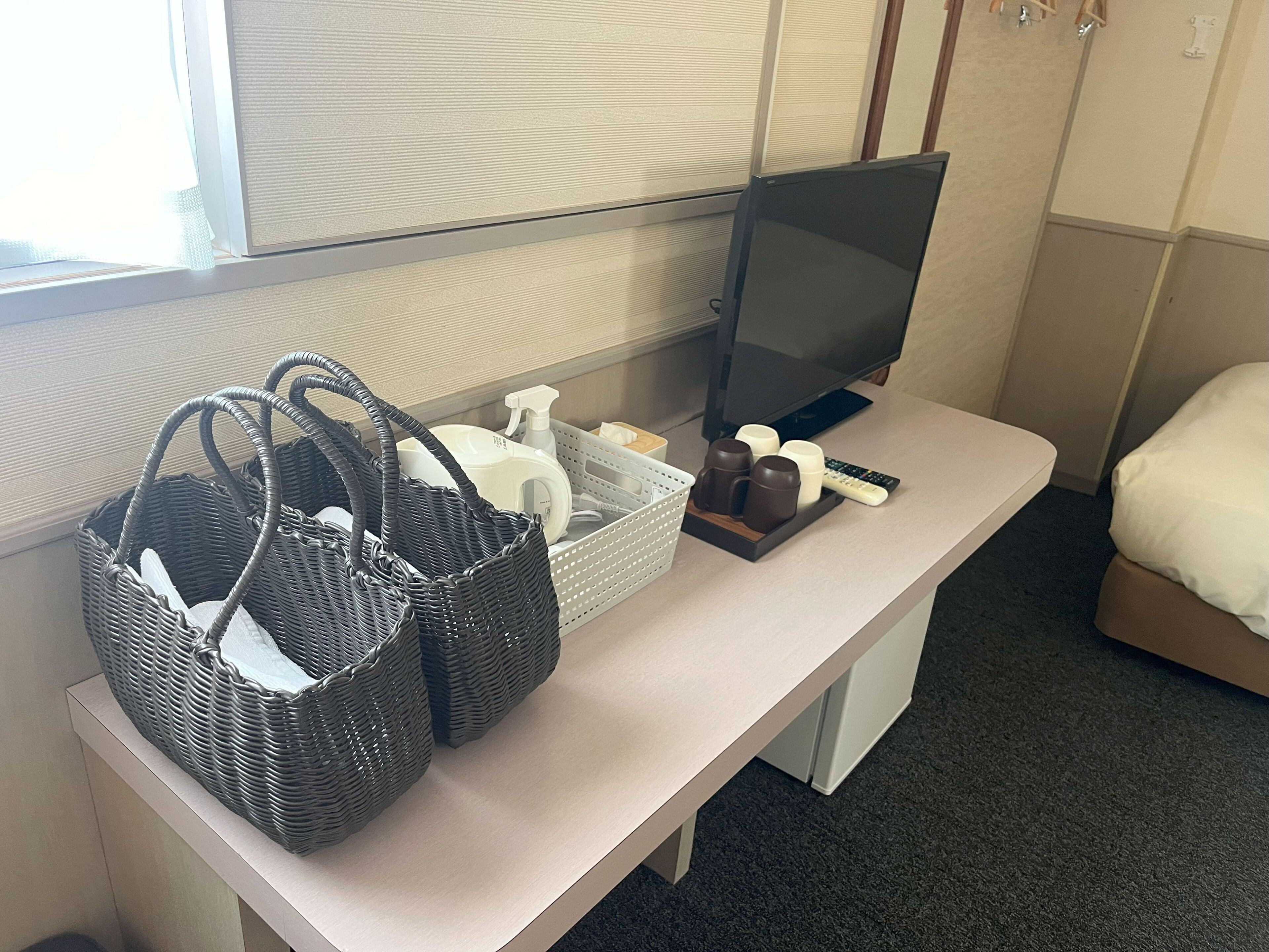 Quarto de hotel com uma mesa, televisão, cesta de produtos de higiene e uma cama.