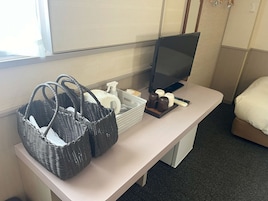 Una habitación de hotel con escritorio, televisor, cesta de artículos de aseo y cama.
