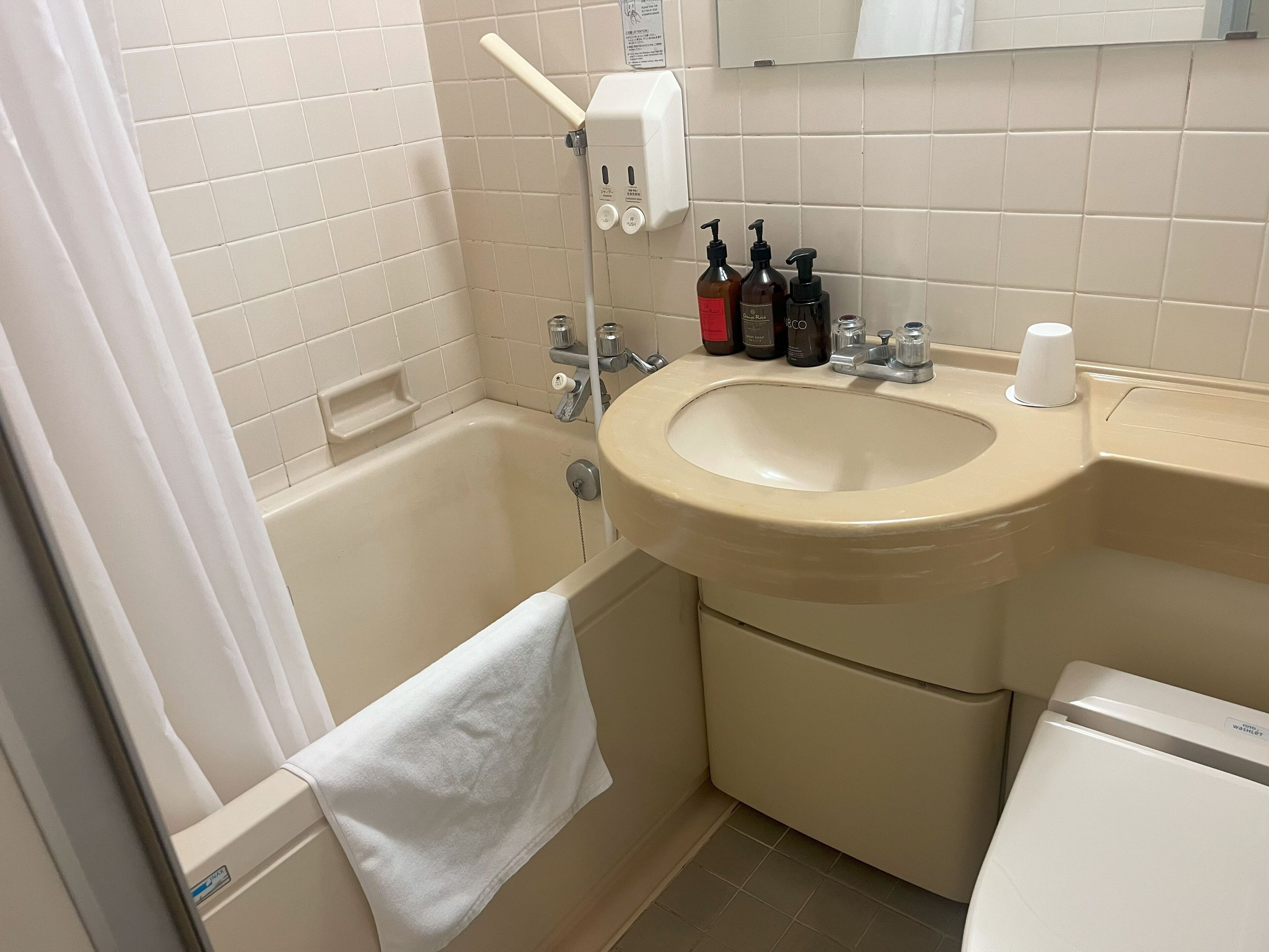 A bathroom with a bathtub, sink, and toilet. There are toiletries on the sink and a towel hanging on the wall.