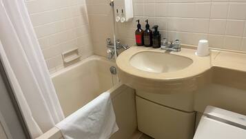 A bathroom with a bathtub, sink, and toilet. There are toiletries on the sink and a towel hanging on the wall.