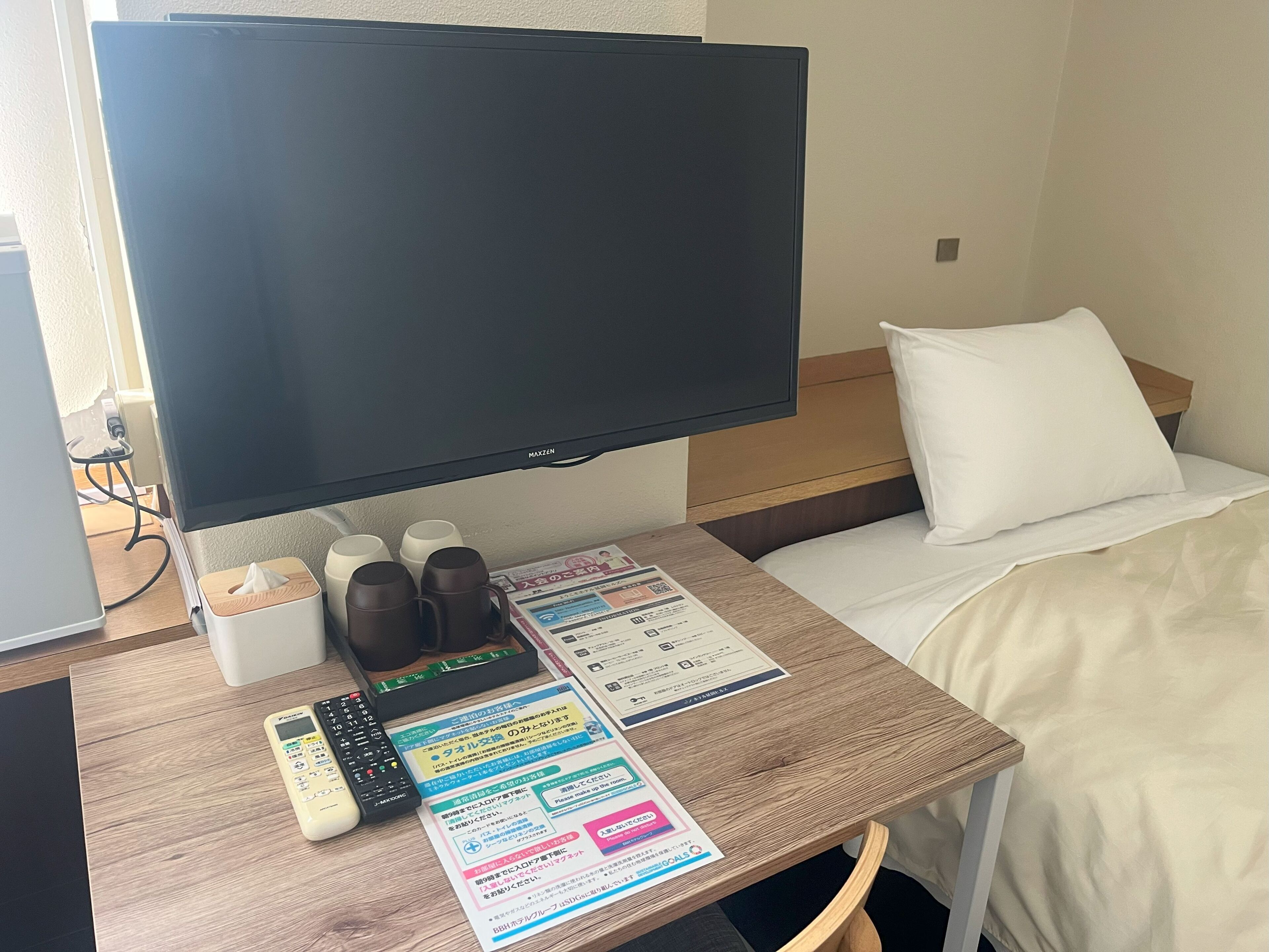 A hotel room with a bed, a TV, a bedside table with a remote control, a tissue box, and a menu.